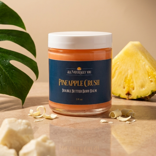 Jar of pineapple crush body balm on a wooden surface with a pineapple and leaves in the background.